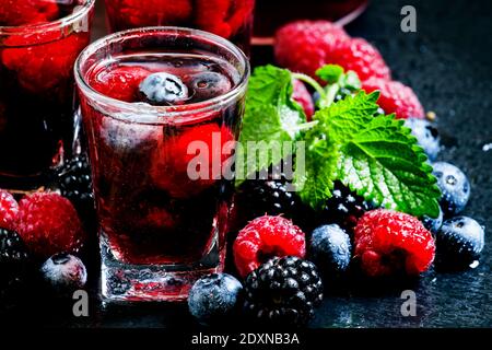 Kalter Sommerbeerentee mit Himbeeren, Heidelbeeren, Brombeeren und Minze in Gläsern auf dunklem Hintergrund, selektiver Fokus Stockfoto