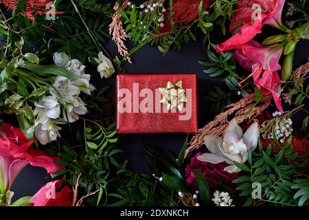 Rote Schachtel mit einem Geschenk, umgeben von Blumen auf einem Dunkler Hintergrund flach lag Stockfoto