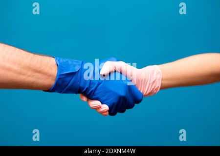 Mann und Frau Hand in Handschuhen treffen in Hand schütteln isoliert auf blauem Hintergrund, Quarantäne Epidemie Konzept Stockfoto