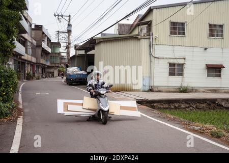 Hsinchu / Taiwan - 20. März 2020: Alter Mann mit Holzbohlen in Motorroller Stockfoto