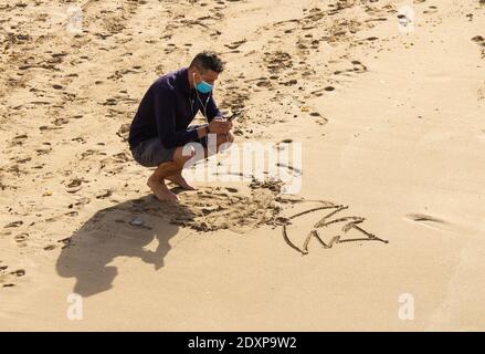 Las Palmas, Gran Canaria, Kanarische Inseln, Spanien. Dezember 2020. Ein Tourist mit Gesichtsmaske fotografiert einen weihnachtsbaum, der am Stadtstrand in Las Palmas auf Gran Canaria im Sand gezeichnet ist; ein beliebtes Winter-/Weihnachtssonneziel für britische Touristen. Kredit: Alan Dawson/Alamy Live Nachrichten Stockfoto