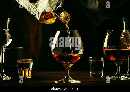 Der Barkeeper gießt den Cognac oder Brandy in ein großes Weinglas an der alten Theke. Vintage Holzhintergrund in Pub oder Bar, Nachtstimmung. Für Text platzieren Stockfoto