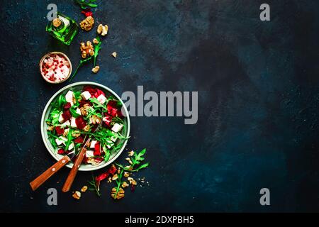 Rucola, Rüben- und Käsesalat mit frischem Radicchio und Walnüssen auf Teller mit Gabel, Dressing und Gewürzen auf blauem Küchentischhintergrund, Platz für te Stockfoto