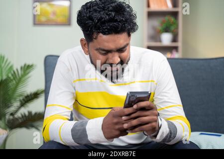 Junger Mann lächelt durch das Lesen lustige Nachricht oder sms auf dem Handy - Konzept der Verwendung von Social Media, Internet und Unterhaltung Lebensstil. Stockfoto