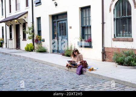 Eine Frau, die von ihrem Computer auf Washington Mews liest, einer privaten eingezäunten Straße in Greenwich Village, Manhattan, New York City Stockfoto