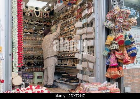 Ein muslimischer Mann in traditioneller Kleidung arrangiert Schmuck zum Verkauf in seinem kleinen Laden-Kiosk. An der 74th Street in Jackson Heights, Queens, New York City. Stockfoto