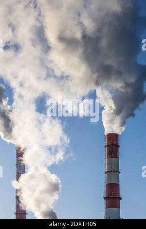 Drei Fabrikrohre mit dichtem Rauch auf blauem Himmel Hintergrund. Luftverschmutzung. Ökologisches Problem. Platz kopieren, vertikale Ausrichtung Stockfoto