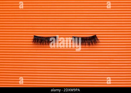 Schwarze False Wimpern Streifen auf orange strukturierten Hintergrund Stockfoto