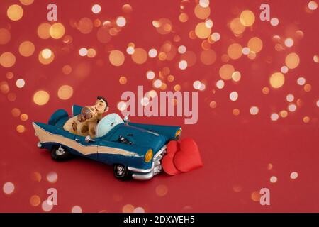 Spielzeug Auto mit einem Paar in der Liebe auf einem roten Hintergrund mit Bokeh Licht Girlanden, Valentinstag. Der Mocap Copyspace. Stockfoto