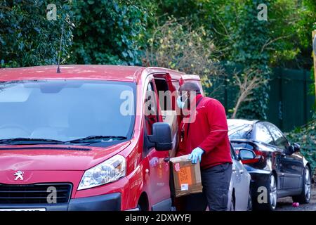 Royal Mail Postbote lädt roten Postwagen mit Paketen für Weihnachtsgeschenk Lieferungen am Heiligabend. Hampstead Royal Mail Delivery Office, London. Stockfoto