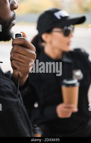 afroamerikanischer Polizist im Radio mit verschwommenem Gespräch Kollege auf Hintergrund im Freien Stockfoto