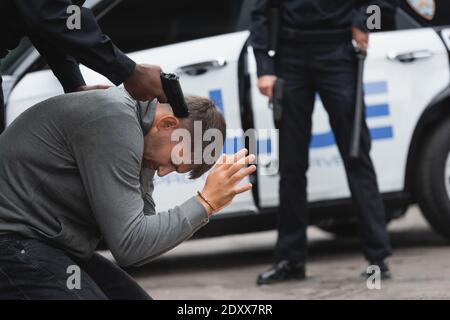 afroamerikanischer Polizist mit Waffe auf Täter mit verschwommen zielen Kollege auf Hintergrund im Freien Stockfoto