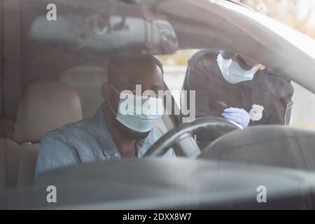 afroamerikanischer Fahrer in medizinischer Maske sitzt im Auto in der Nähe Polizistin auf unscharfem Hintergrund Stockfoto