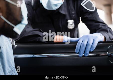 Beschnittene Ansicht des Polizisten in Latexhandschuhen, die in der Nähe von african stehen amerikanischer Fahrer in medizinischer Maske auf verschwommenem Vordergrund im Auto Stockfoto