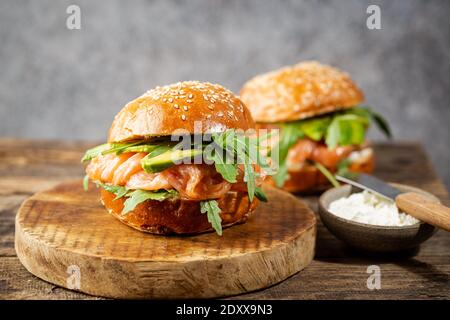 Burger Sandwich mit Lachs, Frischkäse, Avocado und Arugula auf hellem Hintergrund, Konzept Diätkost, Sandwich-Mitnehmen, gesundes Fast-Food Stockfoto