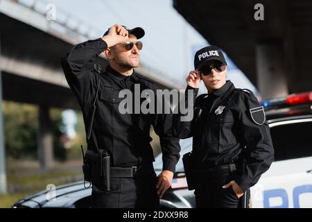 Polizeibeamte in Sonnenbrillen stehen in der Nähe des Autos auf unscharfem Hintergrund Im Freien Stockfoto
