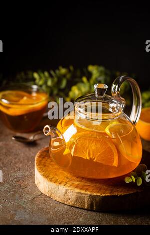 Glas Teekanne mit heißem Zitrustee aus Orangen, Zitronen und Limetten, gesundes Getränk auf dunklem Hintergrund Stockfoto