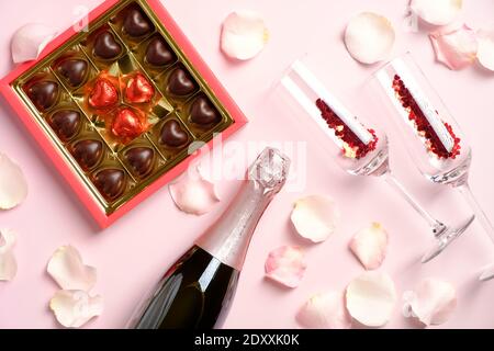 Romantisches Abendessen. Schachtel Pralinen, Flasche Champagner und Gläser mit Konfetti auf rosa Hintergrund mit Rosenblättern verziert. Valentinstag Promi Stockfoto