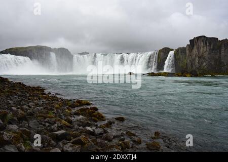 Godafoss Wasserfall in Nordisland vom linken Ufer des Skjalfandafljot Flusses aus gesehen. Dunkelgraue Sturmwolken sammeln sich über dem Wasserfall. Stockfoto