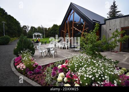 Café Laut in Akureyri Botanical Garden, Nordisland. Die Terrasse mit Stühlen und Tischen vor dem modernen Gebäude ist von Blumenbeeten umgeben. Stockfoto