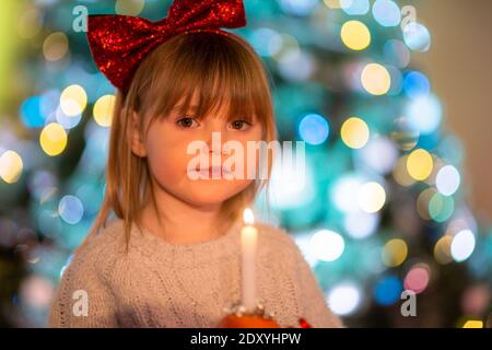 Cradley Heath, West Midlands, Großbritannien. Dezember 2020. Die vierjährige Hermione Hadlington steht stolz mit ihrer Christingle Orange während des Weihnachtsgottesdienstes für Kinder in der Holy Trinity Church, Cradley Heath, West Midlands. Im Christingle-Gottesdienst repräsentiert die Orange die Welt, das rote Band symbolisiert die Liebe und das Blut Christi, die Süßigkeiten stellen alle Schöpfungen Gottes dar, und die brennende Kerze stellt das Licht Jesu in der Welt dar und bringt den Menschen, die in der Dunkelheit leben, Hoffnung. Kredit: Peter Lopeman/Alamy Live Nachrichten Stockfoto