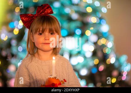 Cradley Heath, West Midlands, Großbritannien. Dezember 2020. Die vierjährige Hermione Hadlington steht stolz mit ihrer Christingle Orange während des Weihnachtsgottesdienstes für Kinder in der Holy Trinity Church, Cradley Heath, West Midlands. Im Christingle-Gottesdienst repräsentiert die Orange die Welt, das rote Band symbolisiert die Liebe und das Blut Christi, die Süßigkeiten stellen alle Schöpfungen Gottes dar, und die brennende Kerze stellt das Licht Jesu in der Welt dar und bringt den Menschen, die in der Dunkelheit leben, Hoffnung. Kredit: Peter Lopeman/Alamy Live Nachrichten Stockfoto