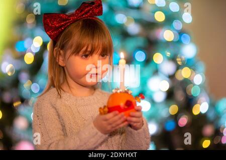 Cradley Heath, West Midlands, Großbritannien. Dezember 2020. Die vierjährige Hermione Hadlington steht stolz mit ihrer Christingle Orange während des Weihnachtsgottesdienstes für Kinder in der Holy Trinity Church, Cradley Heath, West Midlands. Im Christingle-Gottesdienst repräsentiert die Orange die Welt, das rote Band symbolisiert die Liebe und das Blut Christi, die Süßigkeiten stellen alle Schöpfungen Gottes dar, und die brennende Kerze stellt das Licht Jesu in der Welt dar und bringt den Menschen, die in der Dunkelheit leben, Hoffnung. Kredit: Peter Lopeman/Alamy Live Nachrichten Stockfoto