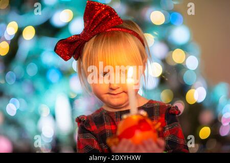 Cradley Heath, West Midlands, Großbritannien. Dezember 2020. Die dreijährige Harlow Hadlington steht stolz mit ihrer Christingle Orange während des Weihnachtsgottesdienstes für Kinder in der Holy Trinity Church, Cradley Heath, West Midlands. Im Christingle-Gottesdienst repräsentiert die Orange die Welt, das rote Band symbolisiert die Liebe und das Blut Christi, die Süßigkeiten stellen alle Schöpfungen Gottes dar, und die brennende Kerze stellt das Licht Jesu in der Welt dar und bringt den Menschen, die in der Dunkelheit leben, Hoffnung. Kredit: Peter Lopeman/Alamy Live Nachrichten Stockfoto