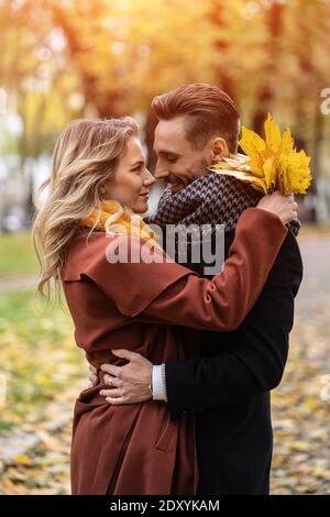 Halblanges Porträt eines küssenden jungen Paares. Ehemann und eine Frau umarmten lächeln einander im Herbstpark zu schauen. Außenaufnahme eines Jungen Stockfoto