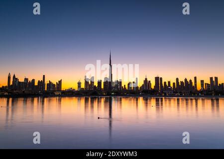 Sonnenaufgang in Dubai mit klarem blauen Himmel Blick vom Boot oder Meer. Morgens geht die Sonne über den Wolkenkratzern der VAE auf. Dubai Strand, Küste, Ufer Stockfoto