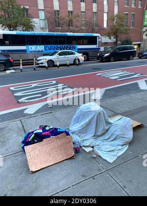 Obdachlose Person schläft unter einer Decke auf dem Bürgersteig, während sie um Hilfe in der 42nd Street nahe dem Grand Central Terminal in Midtown Manhattan bettelt. Stockfoto