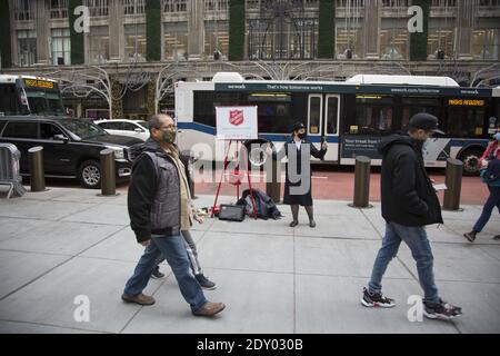 Maskierte und arbeitende Heilsarmee Glockenläuferin, die während der Weihnachtszeit Geld für die Wohltätigkeitsorganisation vor dem Rockefeller Center auf der 5th Avenue anhebt. Stockfoto