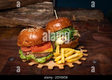 Auf einem dekorativen Holzteil eines einfachen Mechanismus werden eine Doppelte Portion frischer Rindfleisch-Burger und eine mit frittierten Walnüssen serviert. Restaurantkonzept Stockfoto