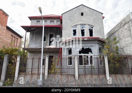 Verlassene zweistöckige Haus mit kaputten Fenstern hinter einem hohen Gitterzaun. Stockfoto