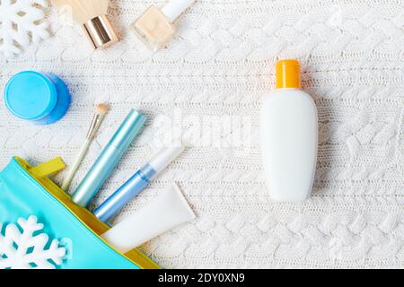 Winterflachlage mit Kosmetik, Sonnenschutzflasche und Schneeflocke auf weißem gestricktem Hintergrund. Stockfoto