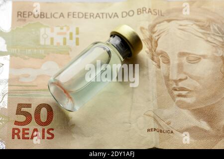 Glas-Impfstoffflasche mit Flüssigkeit über einem brasilianischen '50 Reais' banknote aus der Nähe Stockfoto