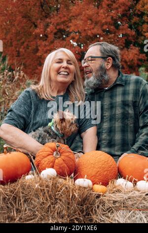 Glückliches älteres Baby Boomer Paar posiert in einer Herbstszene Mit Hund und Pumkins Stockfoto