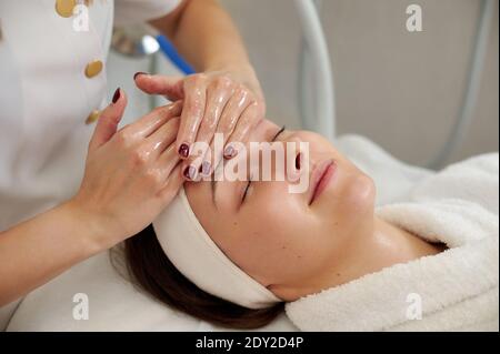 Hände von Kosmetologie Spezialist macht professionelle Gesichtsmassage für schön Junge Frau im SPA-Salon Stockfoto