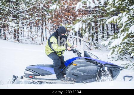 Der Mensch fährt Schneemobil in den Bergen. Pilot auf einem Sportschneemobil in einem Bergwald. Sportler fährt ein Schneemobil in den Bergen. Schneemobil in Stockfoto