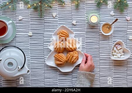 Kreative Xmas Tischaufstellung für Tee mit Kuchen. Kreative flache Lay mit leckeren eclairs oder Braukuchen. Weihnachtsbaum Form Teller mit Kuchen. Tannenzweige Stockfoto