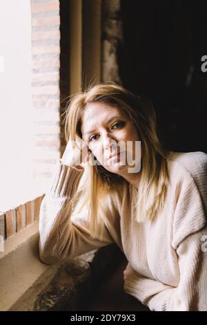 Porträt einer jungen Frau, die in der Nähe des Fensters auf die Kamera schaut Stockfoto
