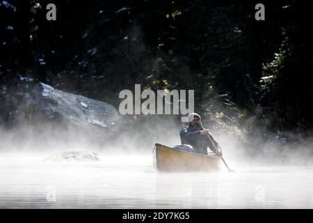 Ein bärtiger Mann mittleren Alters paddelt auf einem nebligen See In Kanada Stockfoto