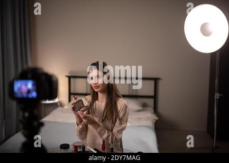 Stilvolle junge Frau demonstriert kompakte Concealer zur Kamera während der Aufnahme Video für Make-up Blog zu Hause Stockfoto