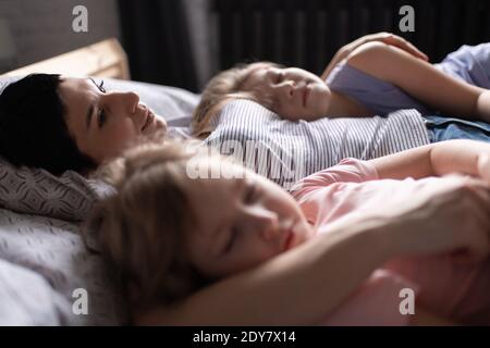 Glückliche Erwachsene Frau umarmt friedlich schlafende Mädchen und ruhen während Morgens im gemütlichen Schlafzimmer auf dem Bett liegen Stockfoto