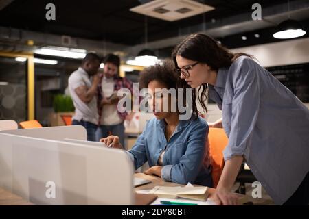 Multiethnische junge Frauen diskutieren während der Arbeit über Daten von einem Laptop Projekt im modernen Coworking Space Stockfoto