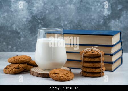 Glas Milch, süße Kekse und Buch auf Marmortisch Stockfoto