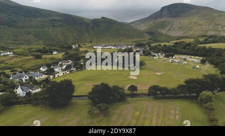 Whiskey-Destillerie im grünen Tal des Berges. Niemand Natur Landschaft im Sommer wolkigen Tag. Schottische Dorf Hütten, Häuser an der Straße Luftaufnahme. Hohe Berge von Arran Island, Schottland. Filmaufnahme Stockfoto