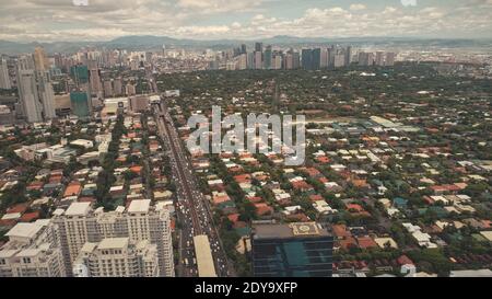 Moderne Wolkenkratzer und Cottages an der Straße mit grünen Bäumen in der oberen Luftaufnahme. Filmische Manila Stadt Stadtbild von Grün städtischen Region Luzon Insel, Philippinen, Asien. Aufnahmen Drohne aufgenommen Stockfoto