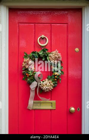 Weihnachtskranz an einer rot bemalten Tür in Chipping campden. Cotswolds, Gloucestershire, England Stockfoto