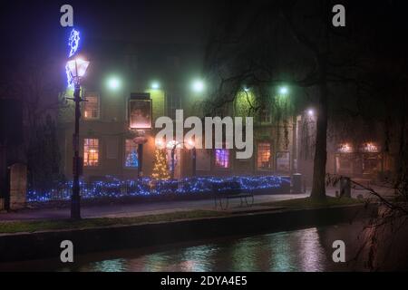 Weihnachtsbaum und Lichter im Nebel vor dem alten Mähne Hotel in der Nacht. Bourton on the Water, Cotswolds, Gloucestershire, England Stockfoto